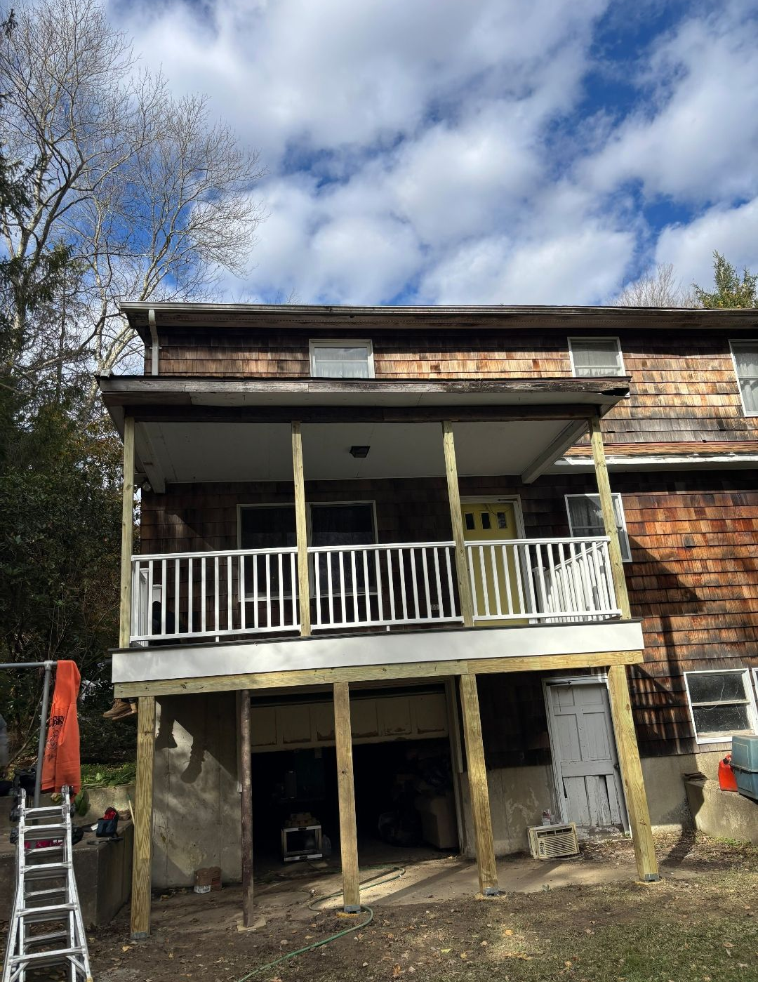 Two-story house with a wooden porch. The porch is supported by beams. Blue sky with clouds in the background.