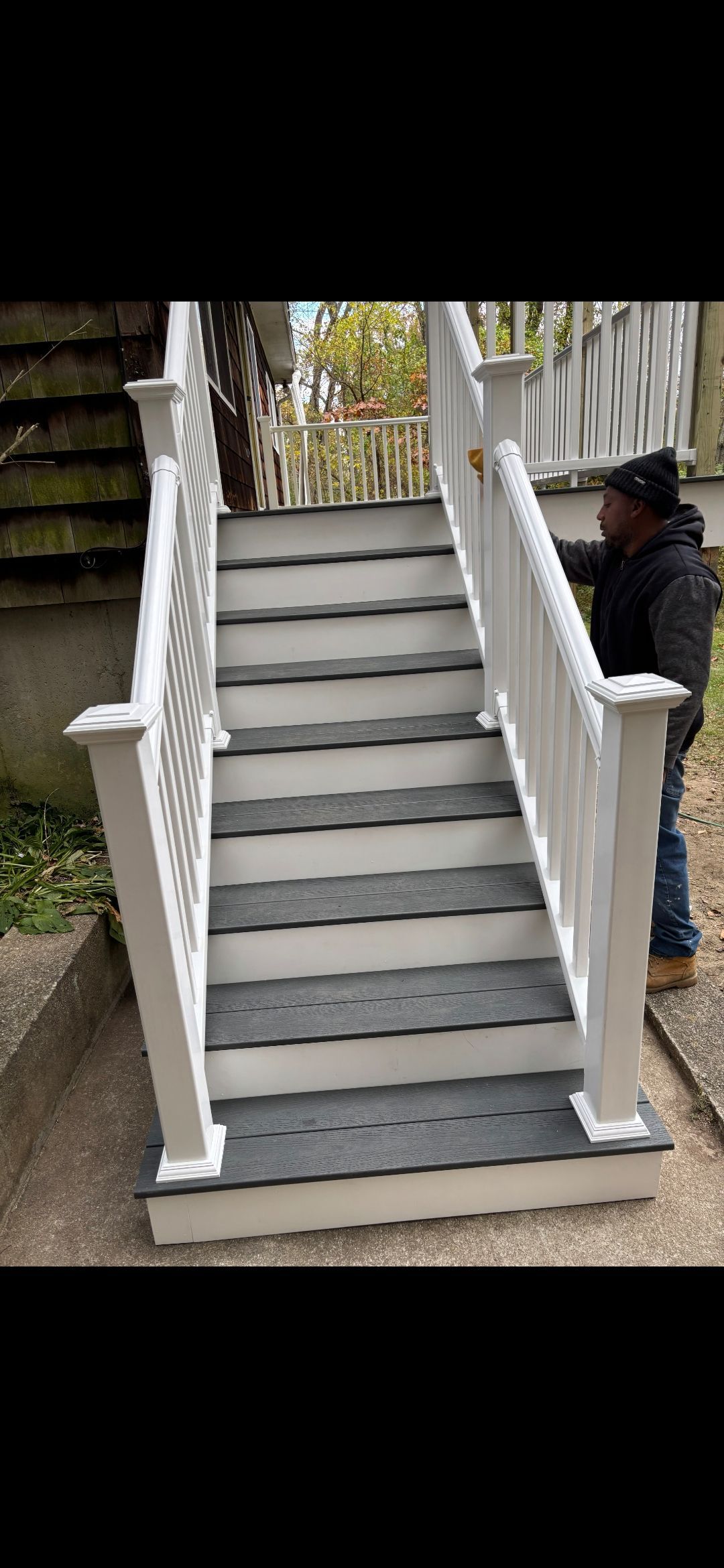 Outdoor staircase with white railing and dark gray steps. Person in a black jacket standing next to the stairs.