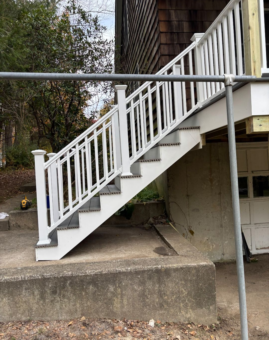White deck stairs with railing against a house, supported by a concrete base.