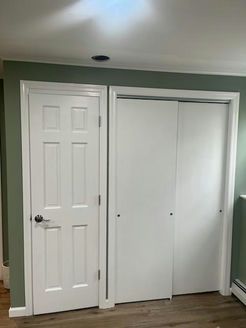 White door and closet doors against green wall, wood-look floor.