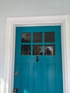 Teal front door with six-pane window, set in white trim. Door is slightly weathered.
