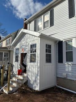 White addition to a house with steps. New construction, windows, siding. Brown earth and blue sky visible.