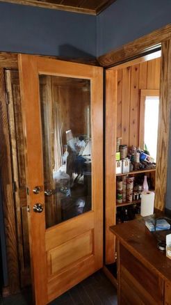 Wooden door with large glass panel, opening into a room with pantry shelves and a wooden dresser.
