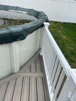 Above-ground pool partially covered, adjacent to a wooden deck with white railing. Green grass visible.