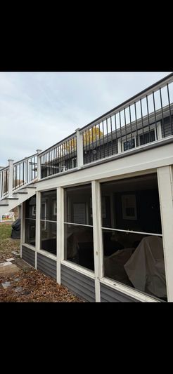 A building with a screened-in porch and a second-story deck. Gray siding, white trim, and a cloudy sky.