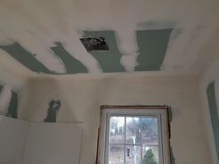 Ceiling drywall installation in a room with a window, unfinished.