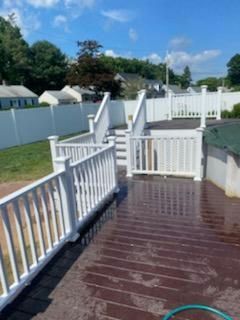 White-railed deck with stairs, leading to a fenced yard, on a sunny day. Brown deck planks.