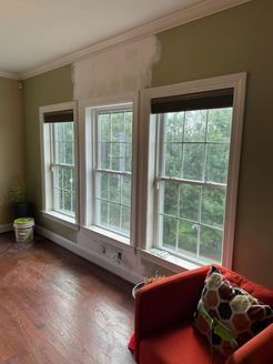 Three windows with white trim in a room with green walls and wood flooring. A red chair sits nearby.