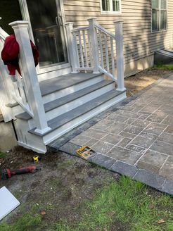 Exterior steps with white railing, leading to a paved patio, beside a siding house.