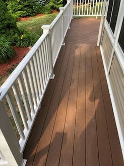 Wooden deck with white railing, brown planks. Sunny outdoor setting.
