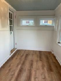 Empty sunroom with light-brown wooden floors, white walls, two windows, and a door. Blue-green ceiling.