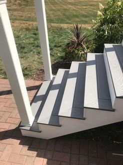 Exterior staircase with grey and white steps, supported by white pillars, leading to a brick patio.