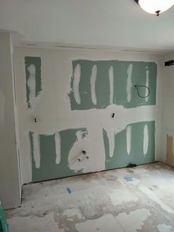 Wall with green drywall patches and white joint compound, in a room under construction.