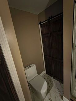 Toilet and dark wood cabinet in a bathroom with tan walls and marble-patterned flooring.