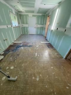 Kitchen renovation in progress: exposed walls, damaged floor, drywall installed, roller visible.