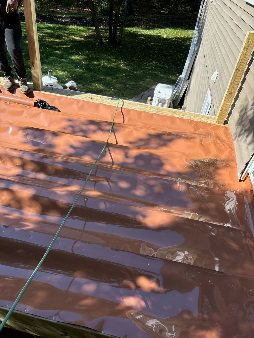 Brown roof being installed, partially covered with reddish waterproof material, person nearby.