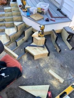 Construction of wooden stairs on a deck with tools and materials scattered around.