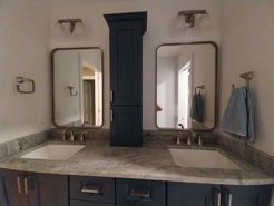 Bathroom with two sinks, mirrors, and a dark blue cabinet. Tan countertop, brown and blue cabinets.
