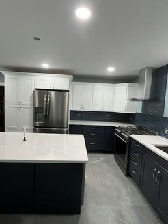 Modern kitchen with white upper cabinets, dark blue lower cabinets, stainless steel appliances, and a white countertop island.