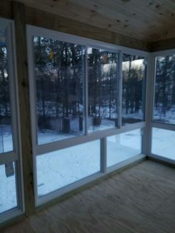 Interior view of sunroom with large windows overlooking a snowy landscape.