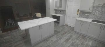 A modern kitchen with grey cabinets, white countertops, and grey tile flooring. An island is in the center.