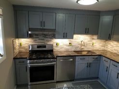 Blue kitchen cabinets with stainless steel appliances and tile backsplash.