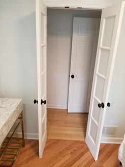 Open white French doors leading into a room with a closed white door and light wood floors.