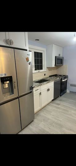 A modern kitchen with stainless steel appliances, white cabinets, and light gray flooring.