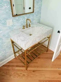 Gold-framed vanity with marble top, gold faucet, and blue wave wallpaper in a bathroom.