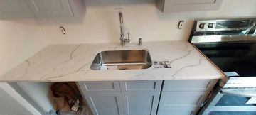 A kitchen countertop with a sink installed. Cabinets are below the countertop. A stove is to the right.