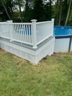 White deck with railing around a partially above-ground swimming pool in a grassy yard.