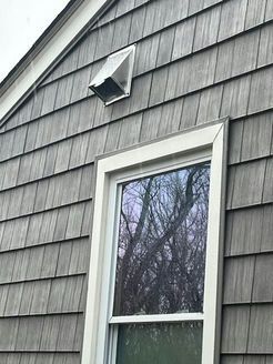Gray shingle siding with white window and vent, tree reflection in window.