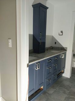 Blue bathroom vanity with tall storage cabinet. White walls, gray countertop and floor.
