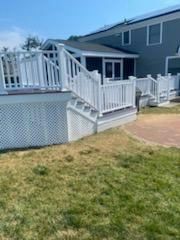 White deck with stairs, lattice skirting, and railing, attached to a gray house with a lawn.