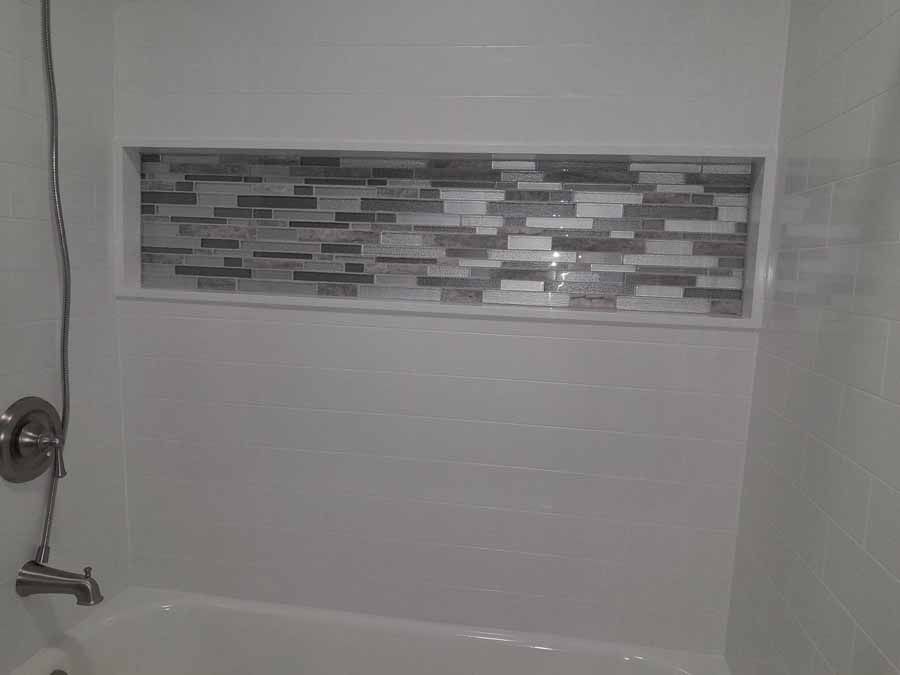 Bathroom with white walls, a built-in shelf with mosaic tile, and a bathtub.