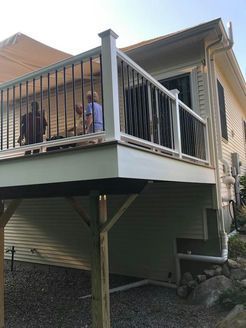 Deck with black railings, white trim, and two people. House exterior with stairs.