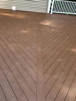 Brown composite deck with angled boards converging at the center, leading to a home with white railing.