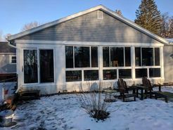 Sunroom addition on a house with large windows, surrounded by snow and a few outdoor chairs.