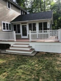 Backyard deck with stairs leading to a sunroom attached to a two-story beige house; green grass in foreground.