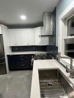 Modern kitchen with white upper cabinets, navy blue lower cabinets, stainless steel appliances, and a gray floor.
