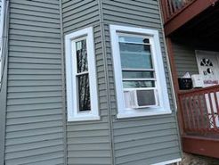 Gray siding with two white-framed windows; one with an AC unit.