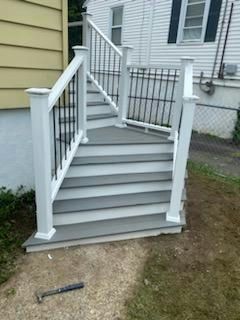 Gray and white outdoor stairs with black railing leading to a white house.