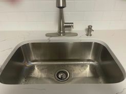 Stainless steel kitchen sink with faucet, soap dispenser, and white countertop.