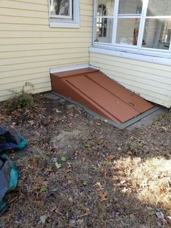 Brown cellar doors set into the side of a yellow house. The doors are angled, leading downwards.