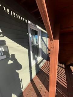 A window on a pale green house, with a brown deck and post. The sun casts shadows.