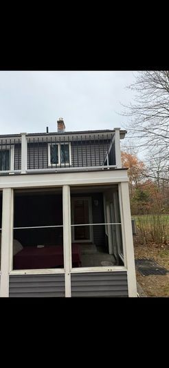 A two-story house with a porch. The house has a gray exterior and a chimney on the roof.