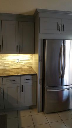 Gray kitchen cabinets with stainless steel refrigerator and tile backsplash.