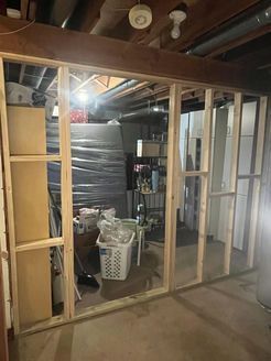 Framing for a new wall in a basement, showing unfinished wood structure. Storage and utilities visible in the background.