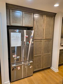 Stainless steel refrigerator and pantry cabinets in a kitchen, with wood flooring.