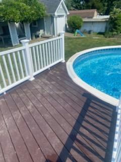 Wooden deck with white railing next to a blue swimming pool. A garage is in the background.